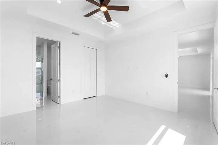 Unfurnished bedroom with a tray ceiling, ceiling fan, a closet, recessed lighting, and light marble finish floors