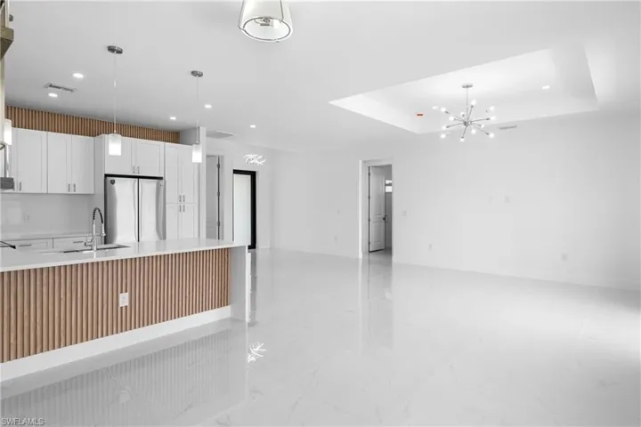 Kitchen with white cabinetry, freestanding refrigerator, a chandelier, light stone counters, and light marble finish floors