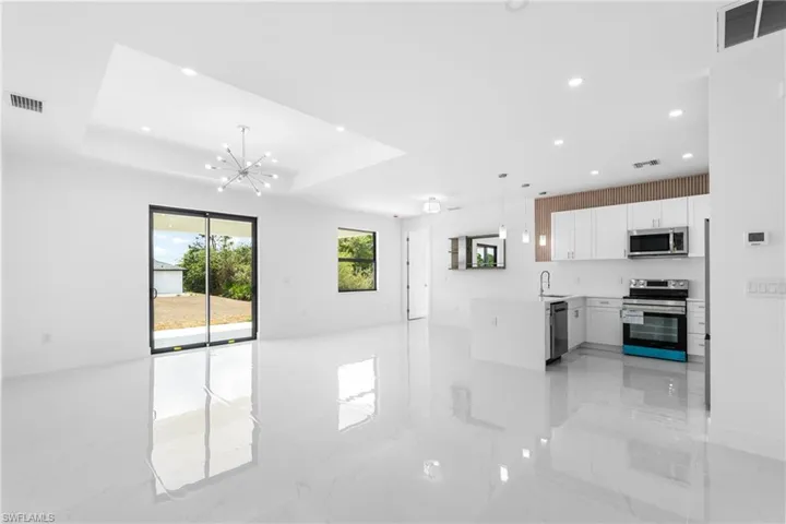 Kitchen with open floor plan, stainless steel appliances, white cabinetry, hanging lights, and light stone counters
