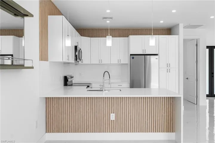 Kitchen with stainless steel appliances, white cabinetry, light stone countertops, and a peninsula