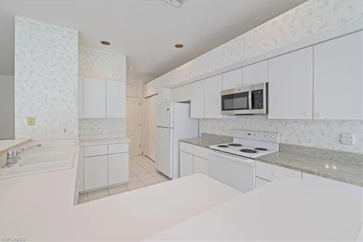 Kitchen featuring wallpapered walls, white cabinetry, white appliances, light countertops, and light tile patterned flooring