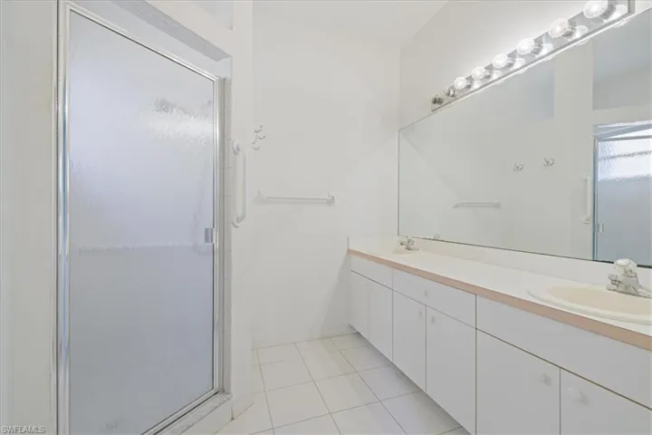 Bathroom with double vanity, a shower stall, and light tile patterned floors