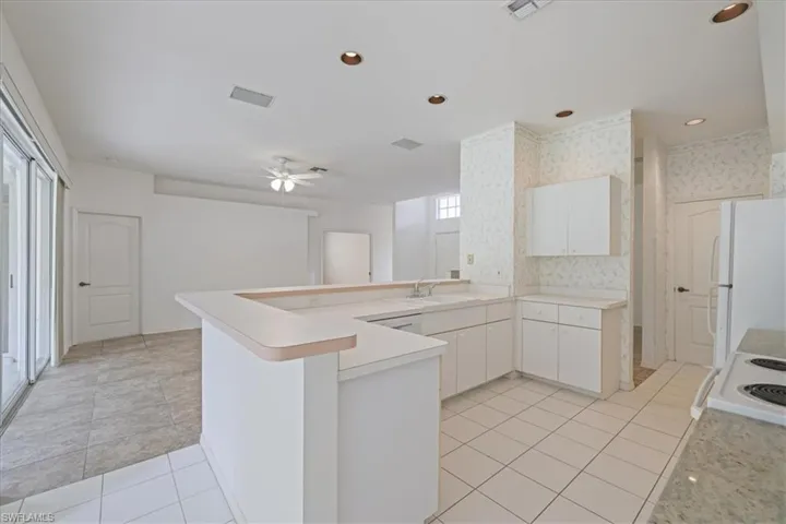 Kitchen with light countertops, white cabinets, a peninsula, white appliances, and recessed lighting