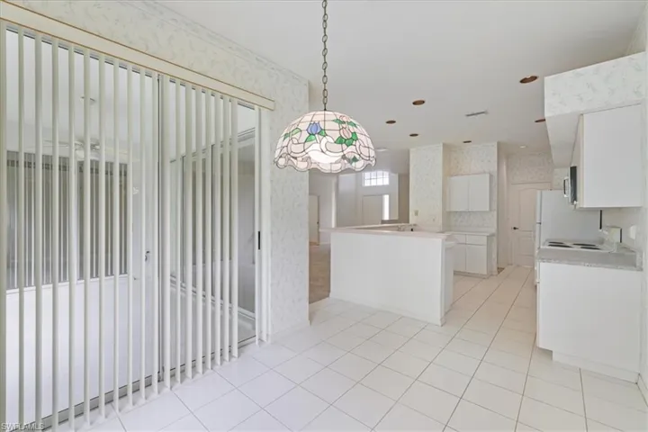 Kitchen featuring wallpapered walls, white cabinetry, light countertops, pendant lighting, and light tile patterned flooring
