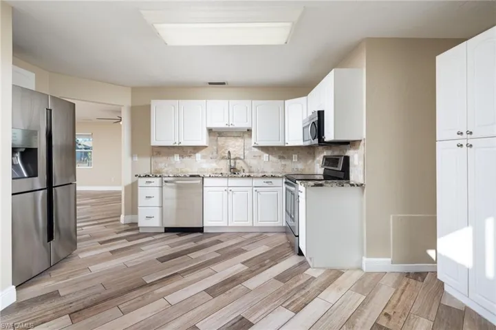 Kitchen with granite counters, stainless steel appliances, light wood-style flooring, white cabinets, tasteful backsplash and large pantry cabinet.