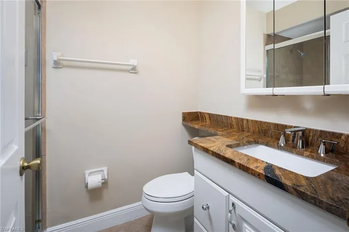 Full bath with granite counter and white vanity, shower with door.