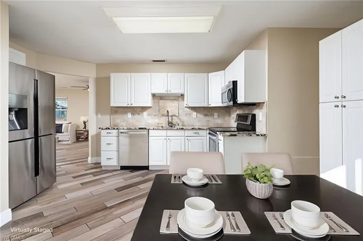 Kitchen with stainless steel appliances, light wood finished floors, light stone countertops, white raised cabinetry, decorative backsplash and large storage pantry.