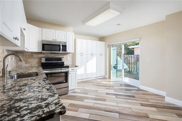 Kitchen with granite countertops, stainless steel appliances, white cabinets, large pantry cabinet and wood plank tile flooring. New slider door with access to side yard.