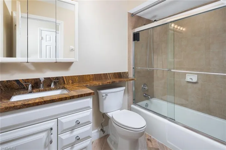 Bathroom featuring granite counter top, white vanity and shower / bath combination with glass door.