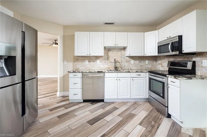 Kitchen with stainless steel appliances, granite counters, wood plank tile floors, and raised white cabinets.
