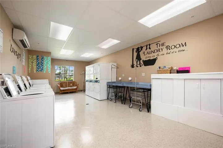 Laundry area featuring a paneled ceiling, a wall mounted AC, cabinet space, and washer and clothes dryer