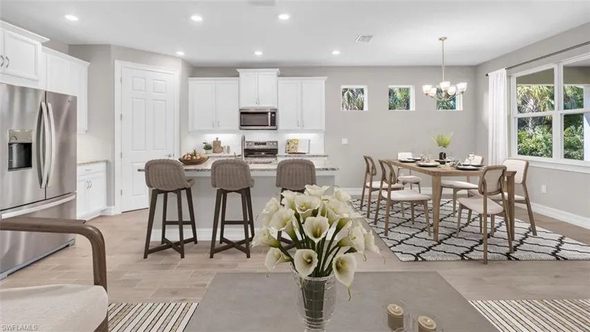 This image is virtually staged. Kitchen with stainless steel appliances, a breakfast bar, white cabinetry, light stone countertops, and a kitchen island with sink