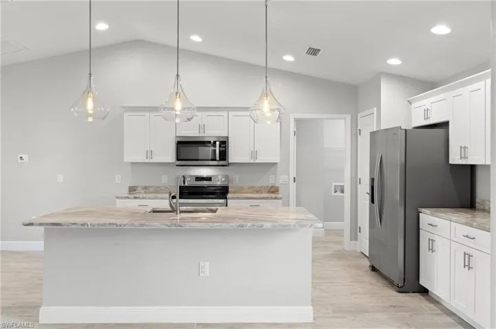 Kitchen with lofted ceiling, a kitchen island with sink, stainless steel appliances, and decorative light fixtures