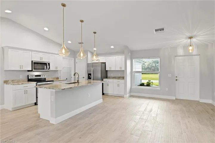 Kitchen featuring white cabinets, decorative light fixtures, stainless steel appliances, and a center island with sink