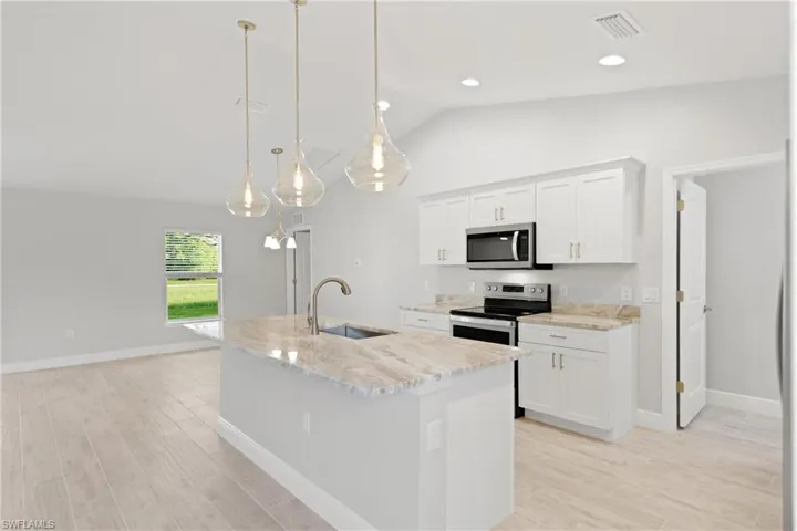 Kitchen featuring hanging light fixtures, vaulted ceiling, an island with sink, appliances with stainless steel finishes, and white cabinetry