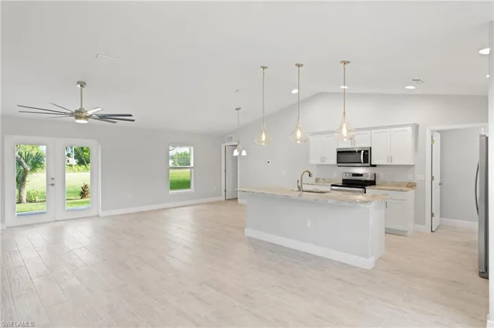 Kitchen featuring light stone counters, stainless steel appliances, pendant lighting, white cabinets, and an island with sink