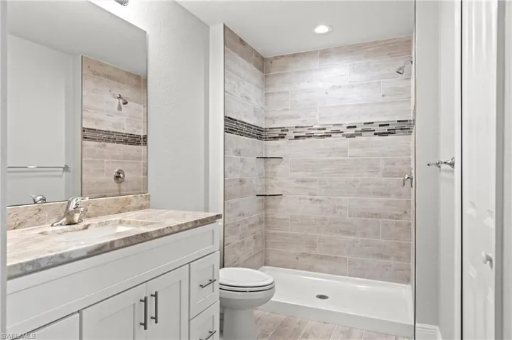 Bathroom featuring a tile shower, toilet, vanity, and hardwood / wood-style flooring
