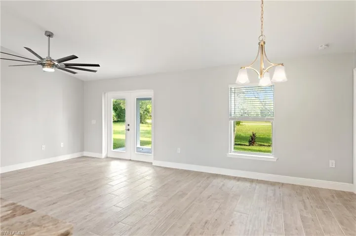 Empty room with french doors, light hardwood / wood-style flooring, and ceiling fan with notable chandelier