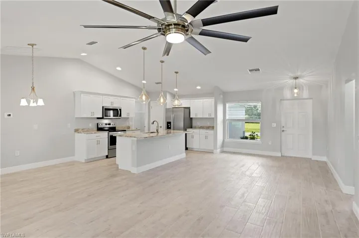 Kitchen featuring white cabinetry, an island with sink, stainless steel appliances, and decorative light fixtures