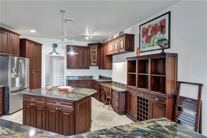 Kitchen with dark stone counters, decorative light fixtures, a kitchen island, visible vents, and stainless steel refrigerator with ice dispenser