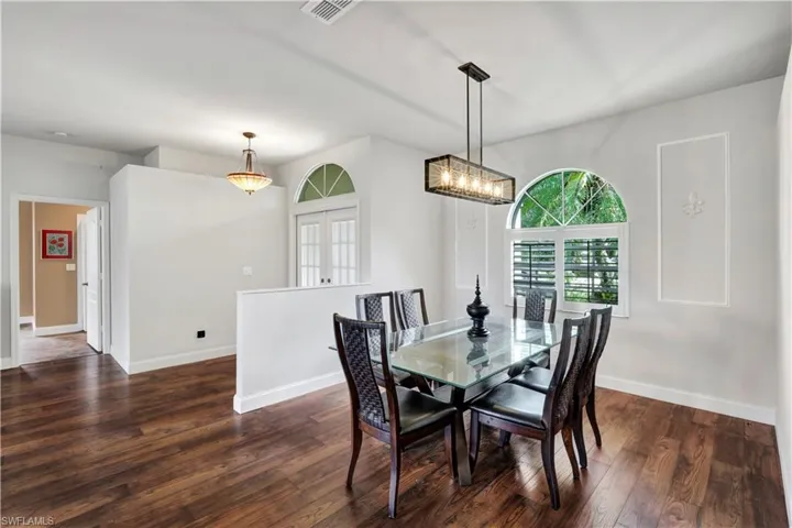 Dining room with an inviting chandelier, visible vents, dark wood-style floors, and baseboards
