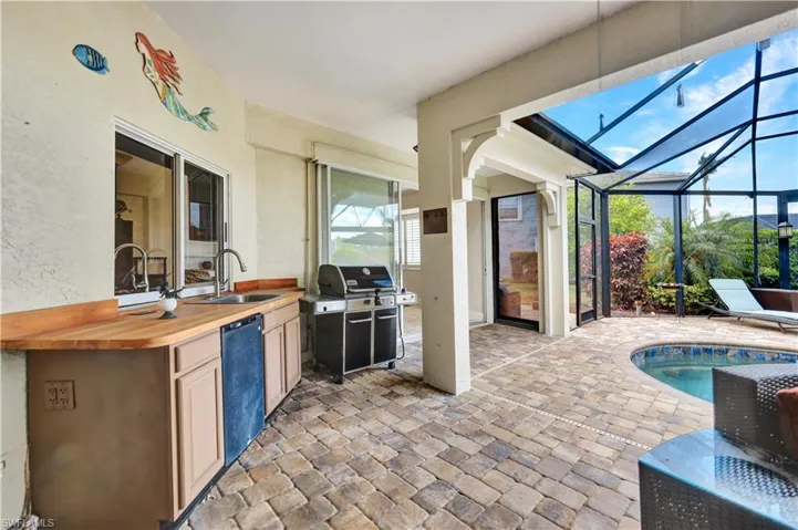 View of patio with glass enclosure, exterior kitchen, grilling area, and a sink