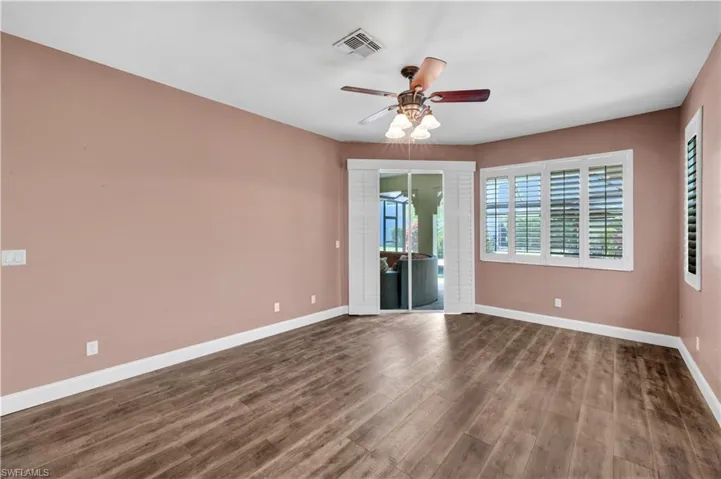 Empty room featuring dark wood-type flooring, a ceiling fan, visible vents, and baseboards