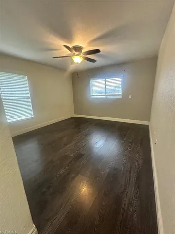 Empty room with a textured wall, a textured ceiling, dark wood finished floors, and ceiling fan