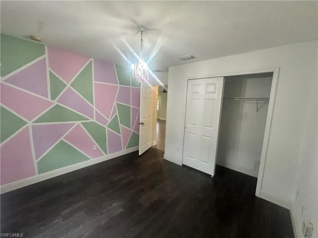 Unfurnished bedroom featuring an accent wall, dark wood-style floors, a closet, a textured ceiling, and wallpapered walls