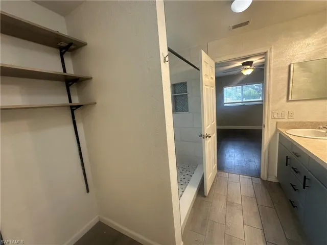 Bathroom with wood tiled floors, a textured wall, a shower stall, vanity, and a ceiling fan