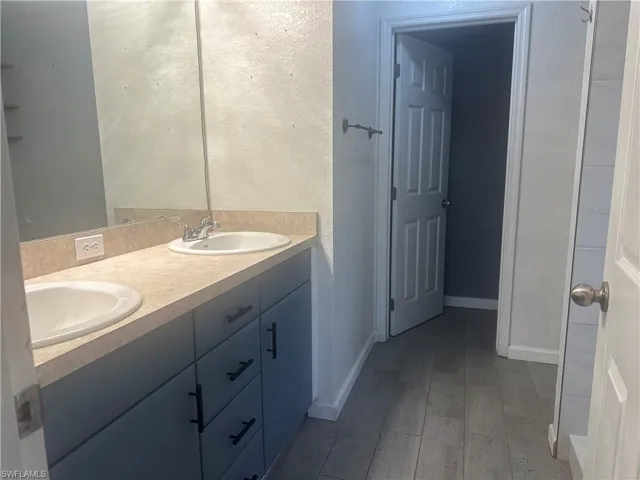 Bathroom with double vanity, light wood finished floors, and a textured wall