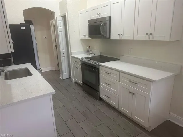 Kitchen with stainless steel appliances, light stone countertops, arched walkways, white cabinetry, and wood tiled floors
