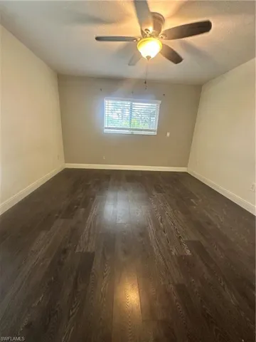 Empty room with ceiling fan, dark wood-type flooring, and a textured ceiling