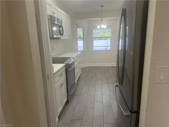 Kitchen with white cabinetry, a textured wall, stainless steel appliances, wood finish floors, and suspended lighting