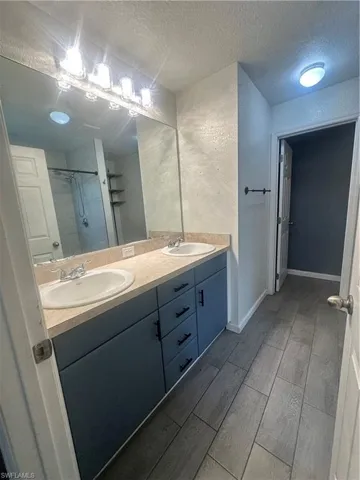 Full bath with double vanity, a shower stall, a textured ceiling, wood tiled floors, and a textured wall