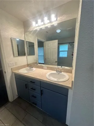 Bathroom featuring a textured wall, double vanity, a textured ceiling, and a shower