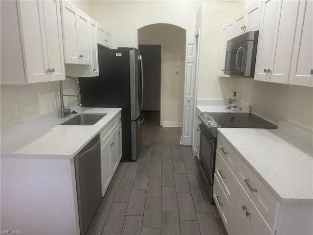 Kitchen with white cabinetry, stainless steel appliances, light stone countertops, wood finish floors, and a textured wall
