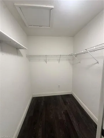 Walk in closet with dark wood finished floors and attic access