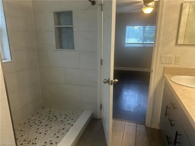 Full bathroom featuring light wood-style flooring, a stall shower, vanity, ceiling fan, and a textured wall