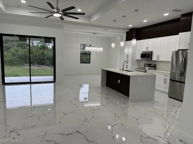 Kitchen with a kitchen island with sink, white cabinets, sink, appliances with stainless steel finishes, and decorative light fixtures