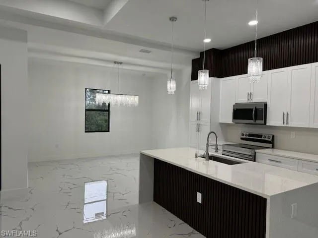 Kitchen with an island with sink, white cabinets, sink, appliances with stainless steel finishes, and decorative light fixtures