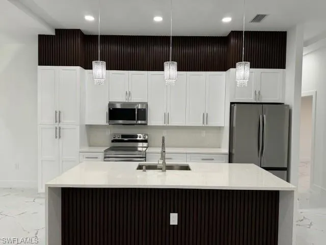 Kitchen with pendant lighting, an island with sink, stainless steel appliances, and sink