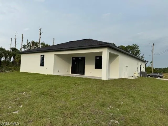 Rear view of house with a lawn and central AC unit
