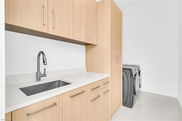 Laundry with light brown cabinets, modern cabinets, light stone counters, and washer and dryer
