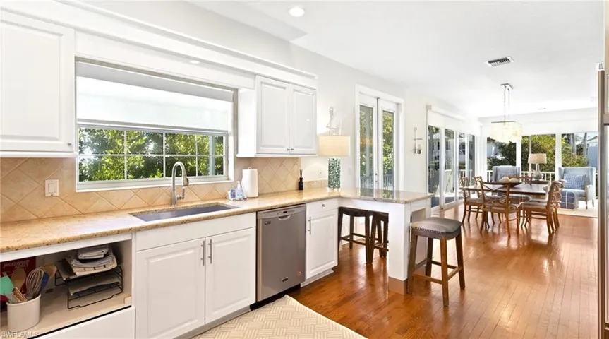 Kitchen featuring dark wood-style flooring, light stone countertops, a breakfast bar, dishwasher, and white cabinetry