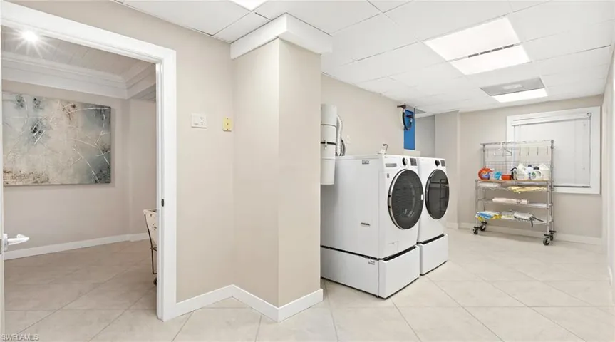 Laundry area featuring independent washer and dryer, light tile patterned floors, and a drop ceiling