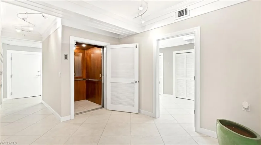Hallway featuring elevator, ornamental molding, light tile patterned floors, and track lighting