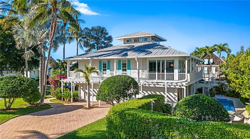 Coastal inspired home with decorative driveway, a standing seam roof, and a balcony