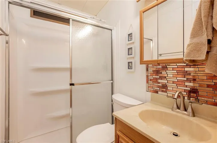Bathroom with decorative backsplash, vanity, toilet, and a shower with shower door