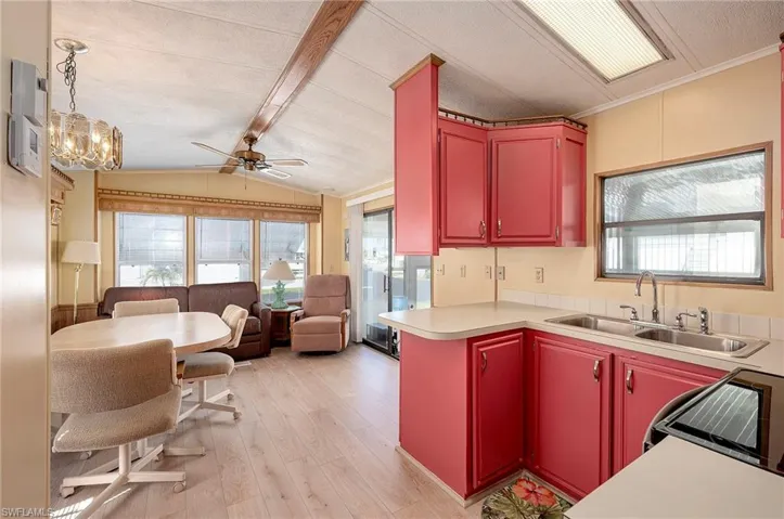 Kitchen featuring lofted ceiling with beams, light hardwood / wood-style floors, sink, ceiling fan with notable chandelier, and ornamental molding